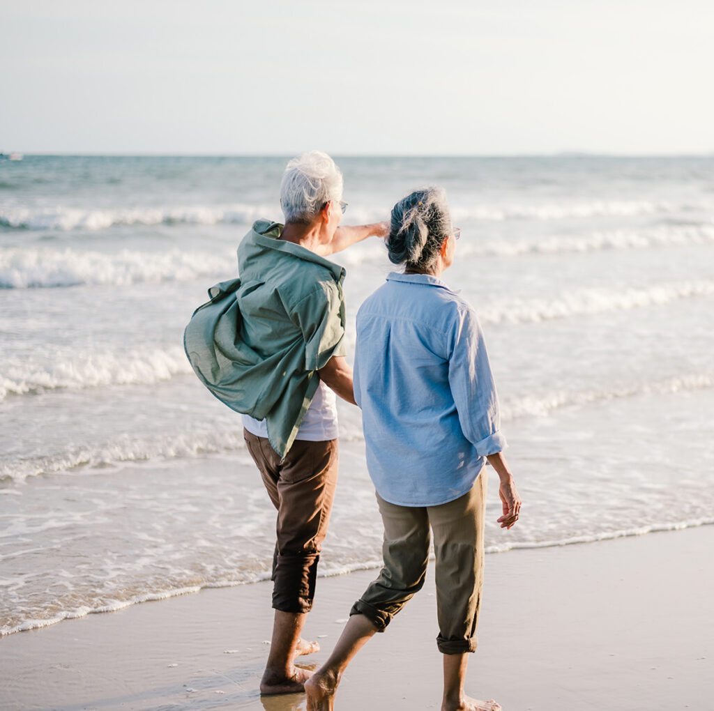 Elderly couple walking on the beach at sunset