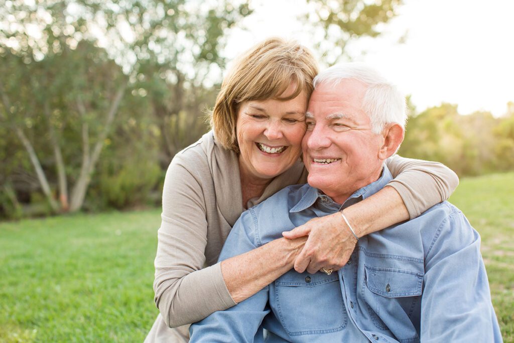 older couple hugging smiling outside at a park