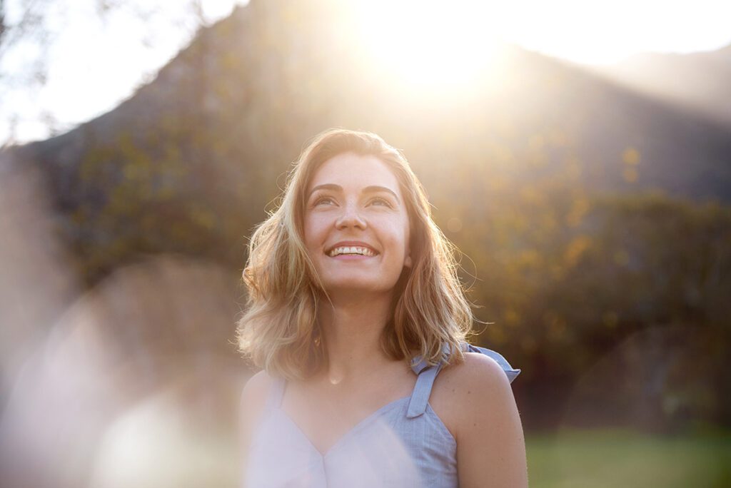 women smiling looking up at the sky with the sun shining in background