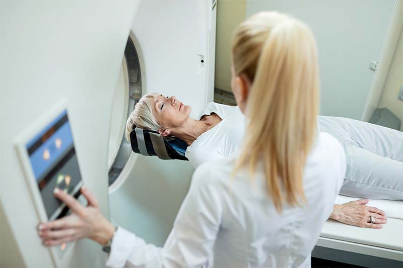 Patient in CT scan machine with radiologist helping